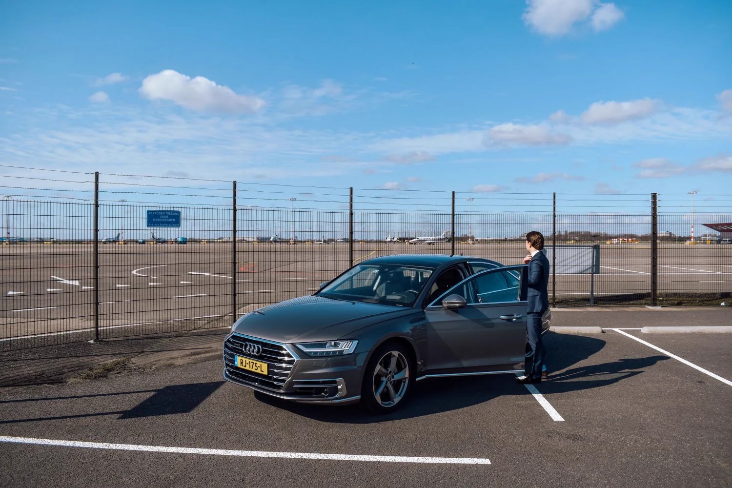 Jonge chauffeur staat klaar met een zakelijke auto bij de luchthaven